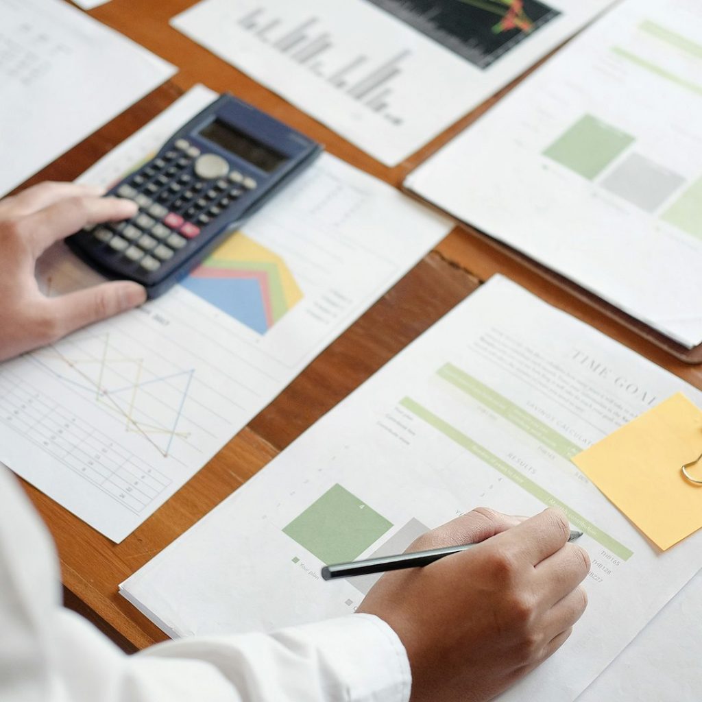 Person wertet Finanzunterlagen und Diagramme mit Taschenrechner und Stift aus – Symbolbild für betriebswirtschaftliche Analysen im Kontext von Betriebsprüfung zur Forschungszulage