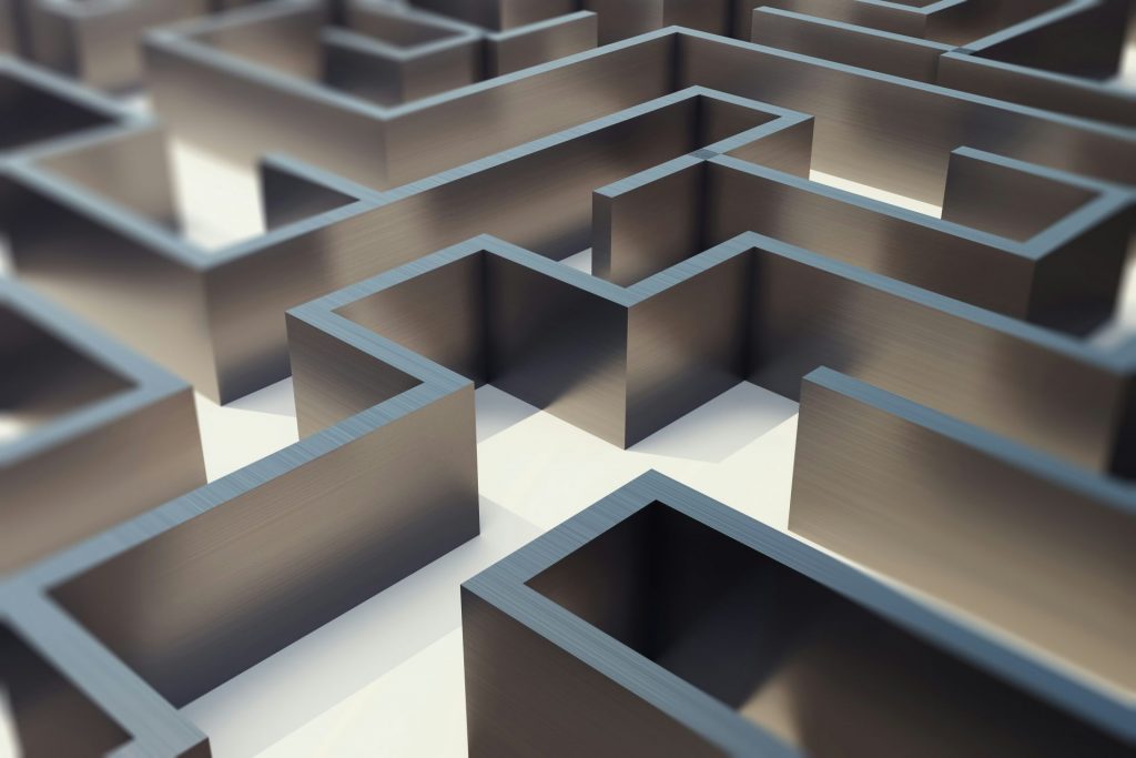 Abstraktes Labyrinth mit metallisch wirkenden Wänden – symbolisiert die komplexen, verschlungenen Wege und Herausforderungen, vor denen kleine und mittlere Unternehmen (KMU) im Zuge der Reform stehen, insbesondere im Bereich der Fördermittelabrechnung und internen Verwaltungsprozesse.