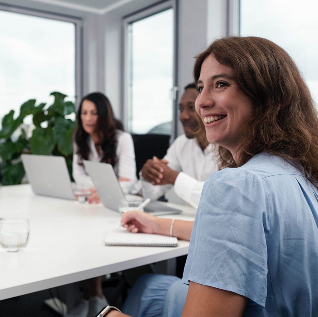 Lächelnde Frau im Gespräch mit Kolleg:innen in einem modernen Büro – symbolisch für persönlichen Kontakt und professionelle Zusammenarbeit bei PFIF