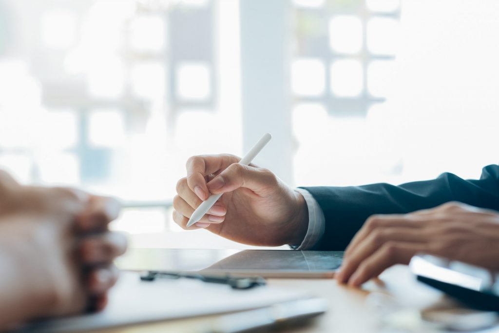 Zwei Personen sitzen an einem Tisch und besprechen Unterlagen, während eine Hand mit einem Stift auf ein Dokument zeigt. Die Szene symbolisiert Beratung und Planung zu Fördermöglichkeiten für KI-Forschung.