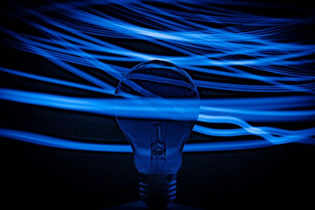 Glühbirne als Symbol für Innovation, umgeben von dynamischen blauen Lichtlinien auf dunklem Hintergrund, steht für kreative Ideen und technologische Entwicklung im Rahmen von Digitalisierungsförderprogrammen.