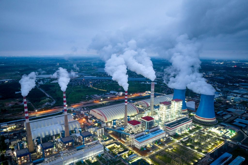 Luftaufnahme eines großen Industrieareals mit mehreren rauchenden Schornsteinen und Produktionsanlagen, das die Notwendigkeit und Bedeutung der Förderung zur Dekarbonisierung der Industrie verdeutlicht.