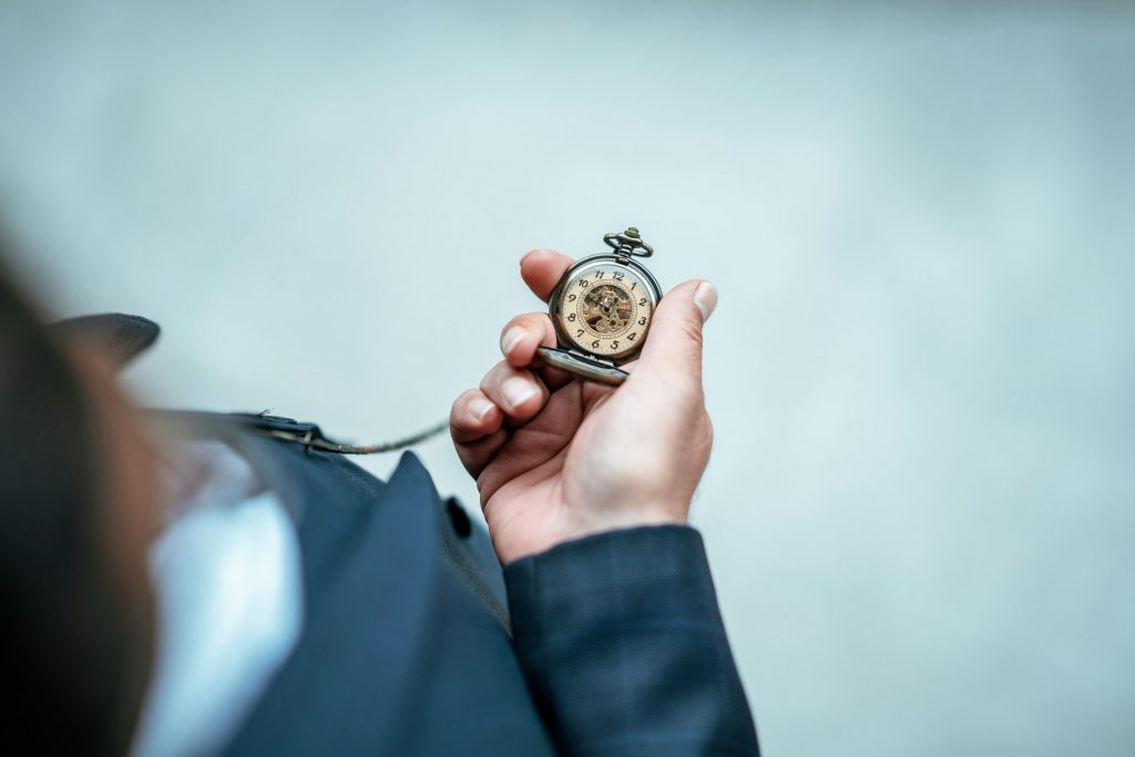 Eine Person in einem Anzug hält eine geöffnete Taschenuhr in der Hand. Die Nahaufnahme symbolisiert die fristgerechte Erstellung und Einreichung eines Zwischennachweis im Rahmen projektbezogener Fördermaßnahmen.