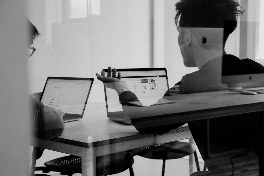 Zwei Personen arbeiten an Laptops in einer Besprechungssituation zur Planung und Abstimmung komplexer Verteidigungsprojekte.