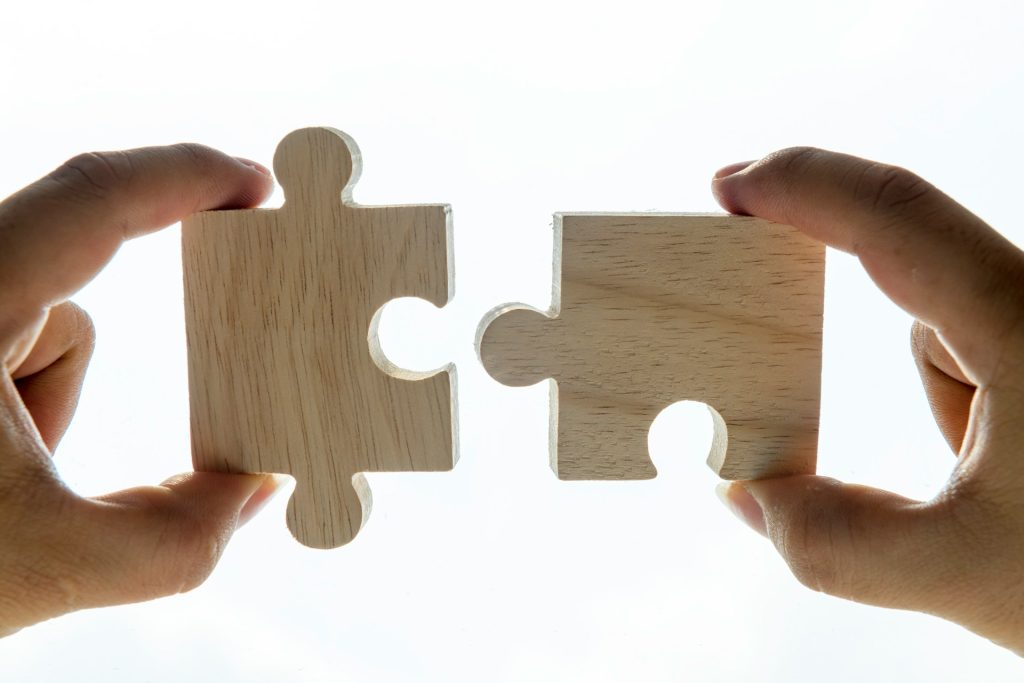 Zwei Hände führen passende Puzzleteile zusammen und symbolisieren die gesellschaftliche Verflechtung sowie die Zusammenarbeit im Kontext der Forschungszulage für verbundene Unternehmen.