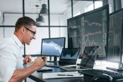 Ein Mitarbeiter sitzt mit Freude vor vielen Monitoren mit Analysen zur Geschäftsentwicklung als Symbol, wie die Forschungszulage in komplexen Unternehmen genutzt wird.